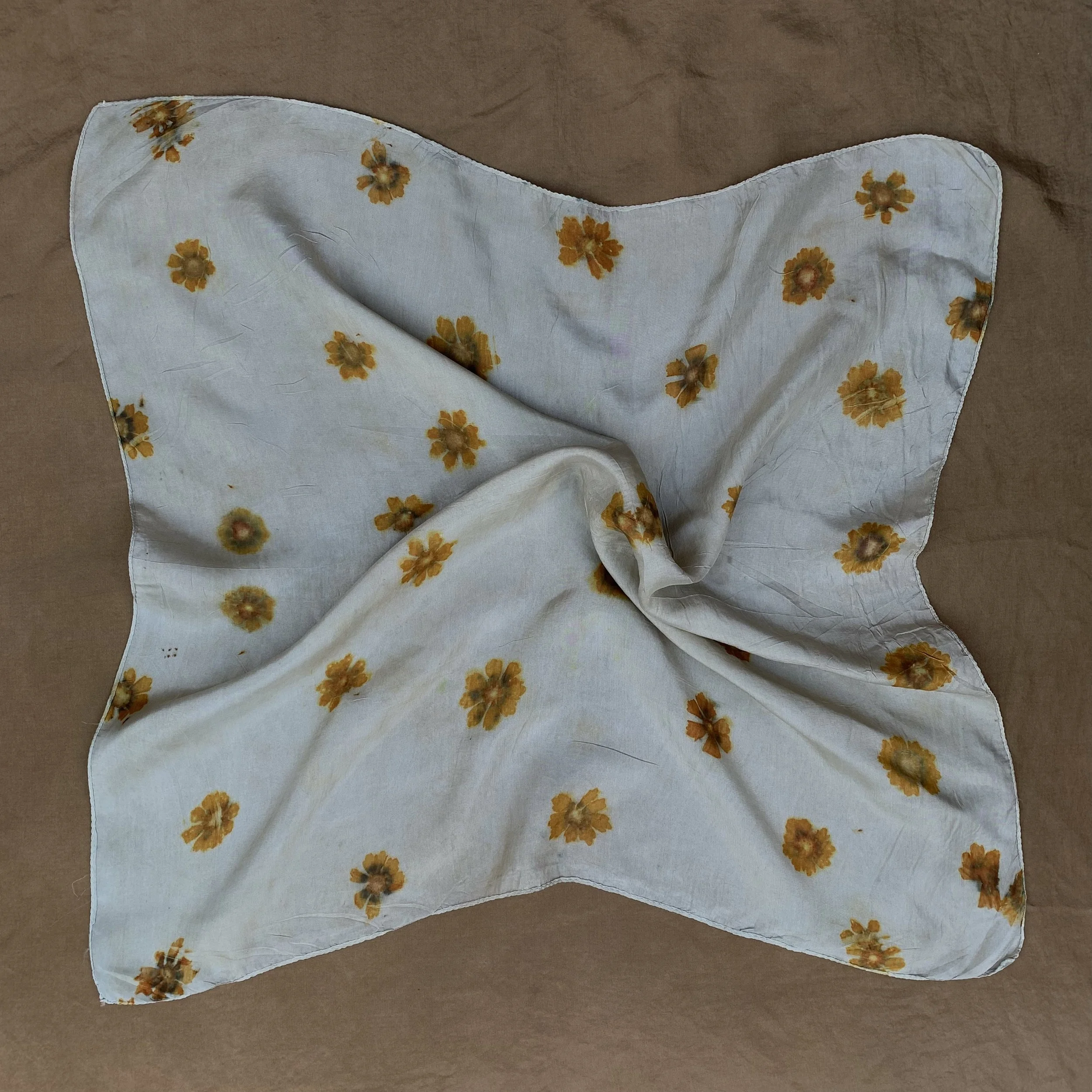 A light brown silk scarf with yellow floral pattern, partially folded, on a brown surface.