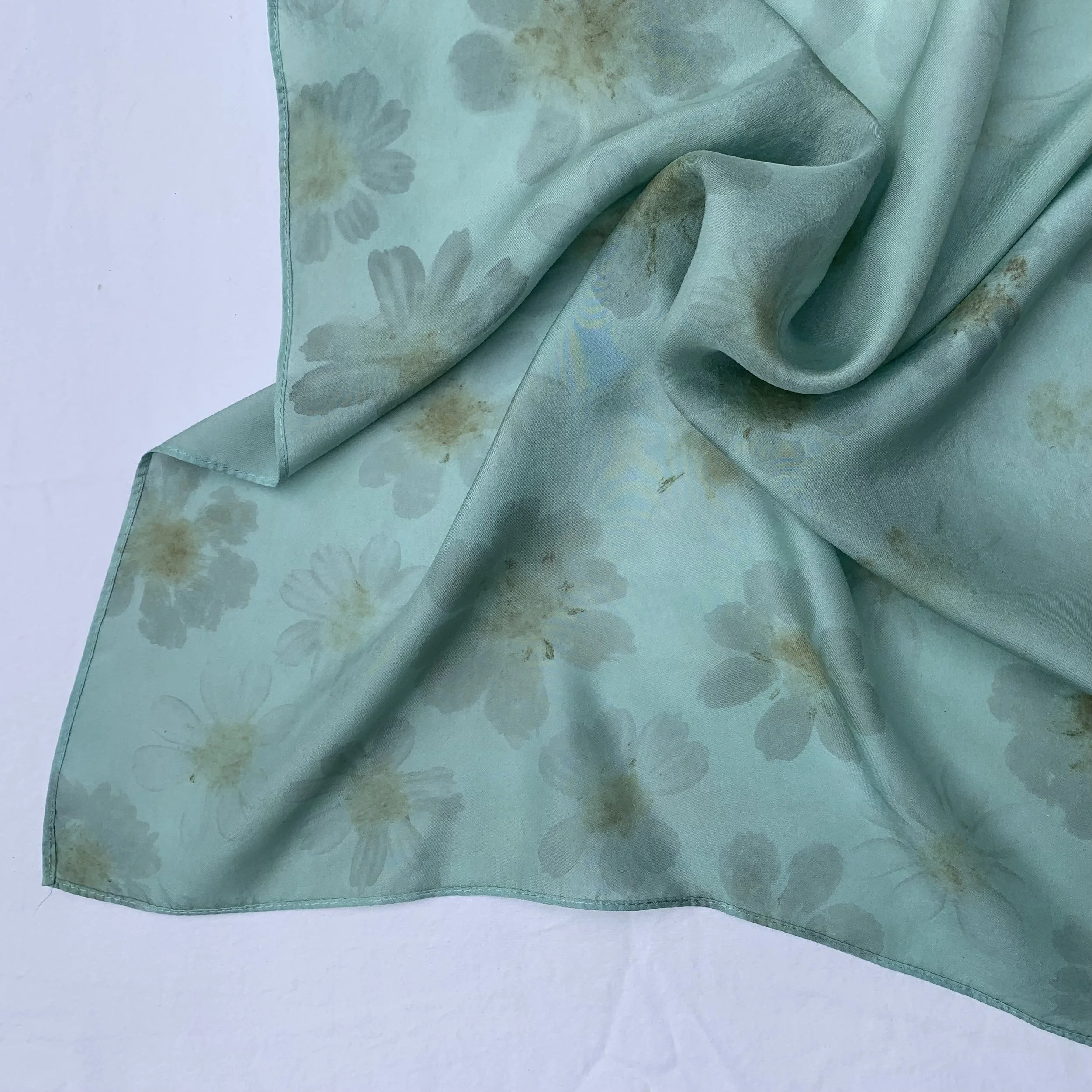 Light blue silk scarf with a daisy flower pattern, slightly wrinkled and draped over a white surface.
