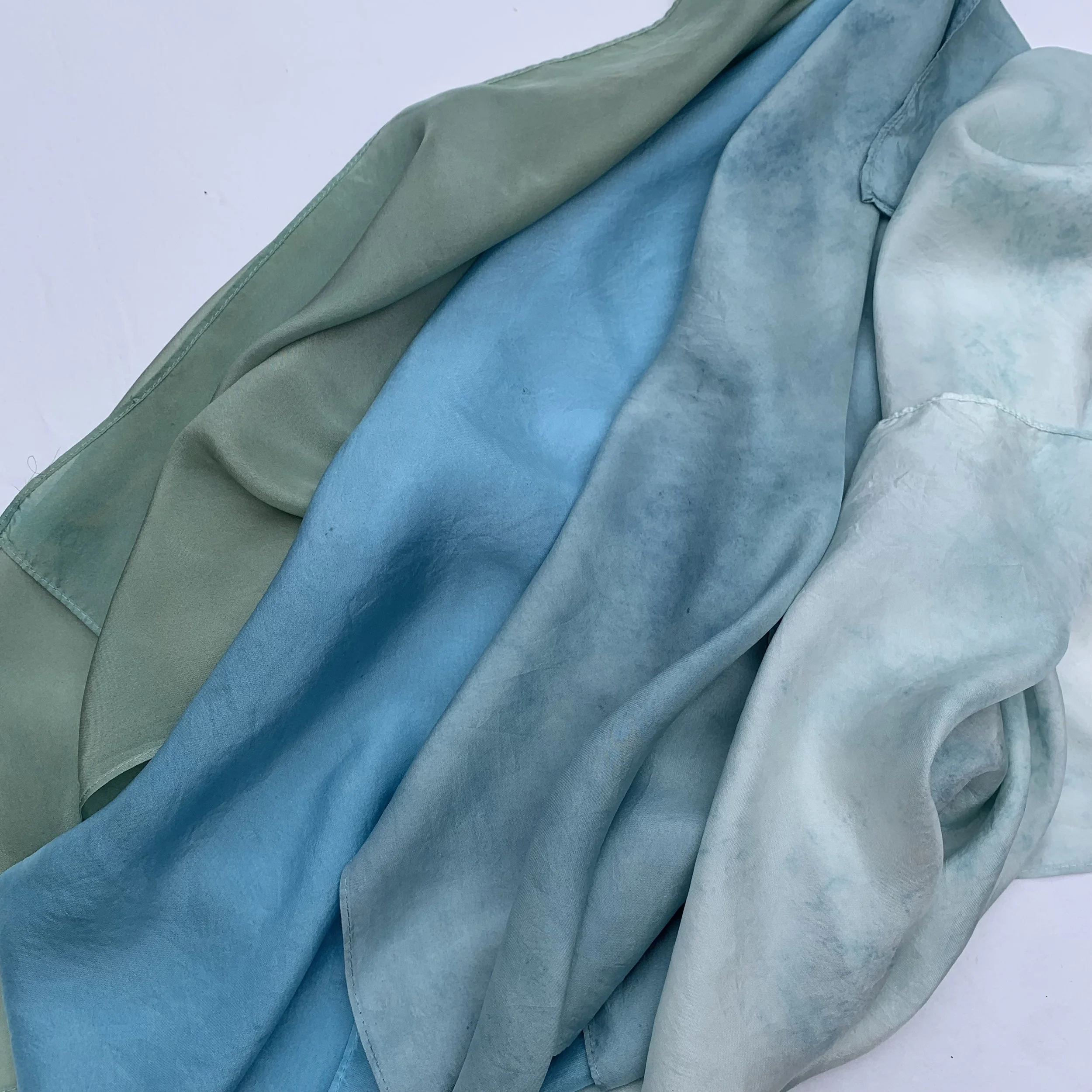 Soft silk scarves in shades of green, blue, and light gray or off-white.