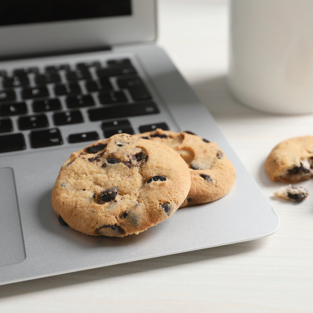 Chocolate chip cookies on a laptop keyboard with a coffee mug nearby.
