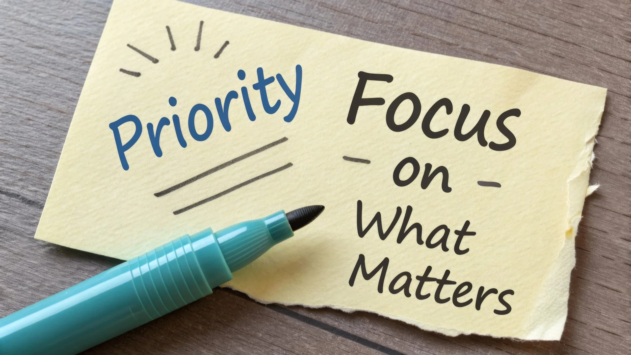 A yellow post it note with the words 'Priority - Focus on what matters' handwritten on it, and a blue marker pen resting on the paper.