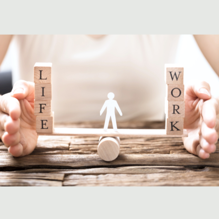 A balance scale made of wooden blocks with the words 'LIFE' on the left and 'WORK' on the right, and a small human figure in the center balancing them.