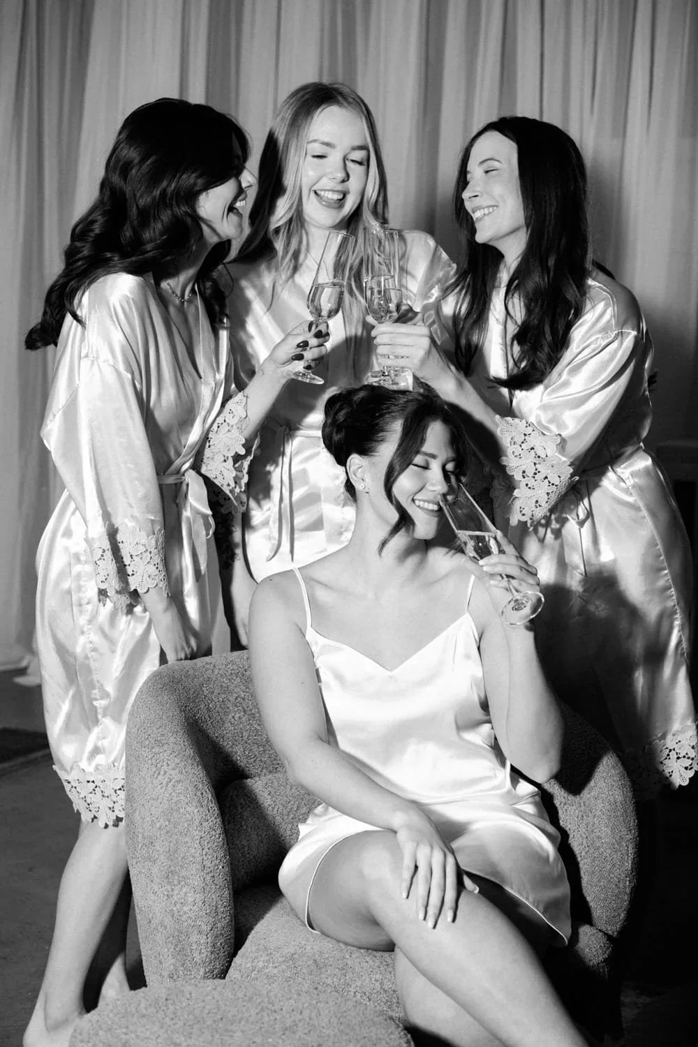Four women in silk robes laughing and cheersing with champagne flutes.