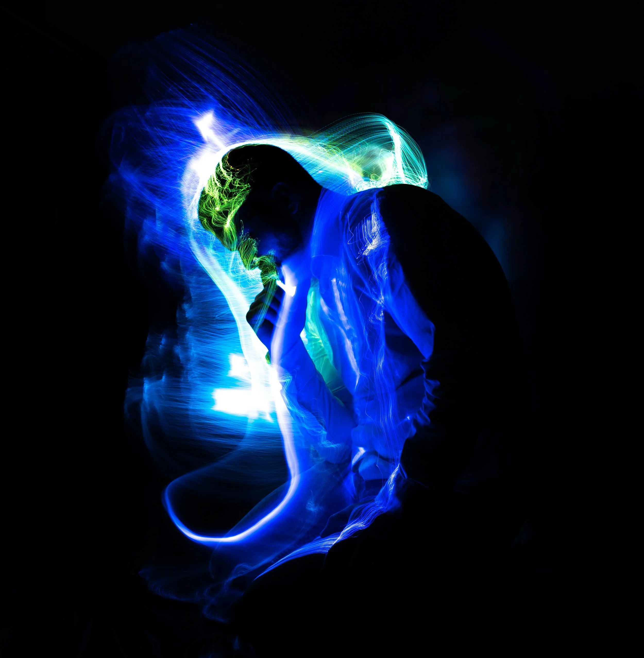 Silhouette of a person with colorful light trails creating a glow around them, set against a black background.