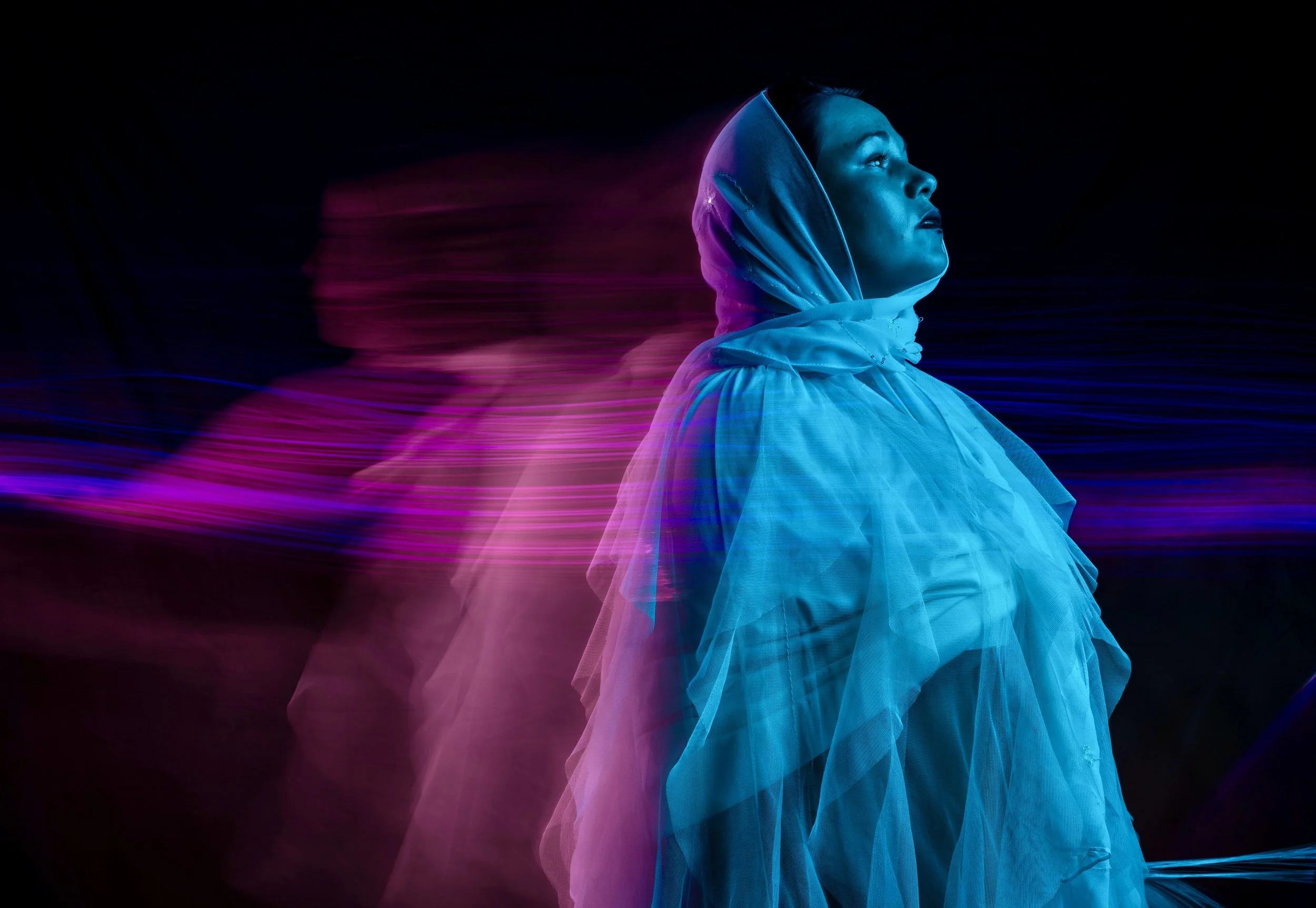 A woman in profile wearing a hooded jacket, illuminated by neon blue and pink lights with motion blur effects.