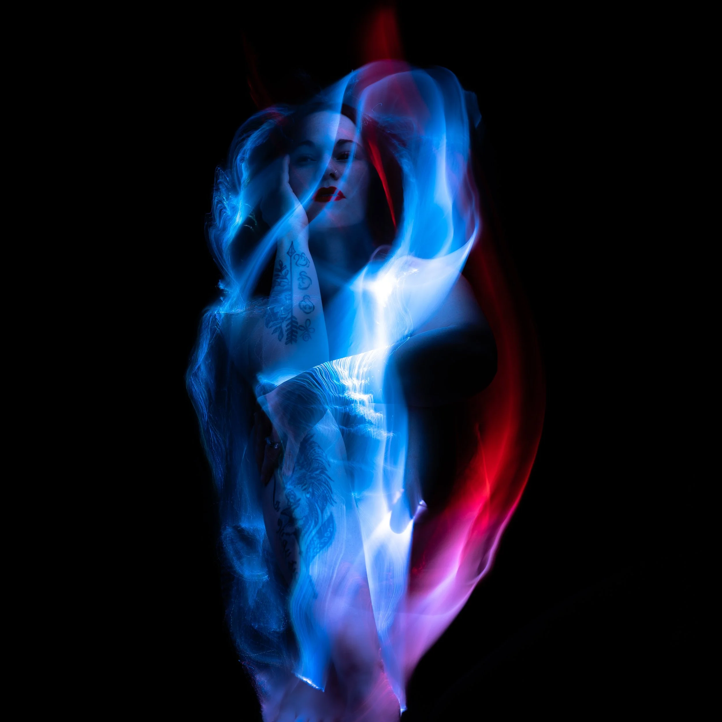 A light-painting portrait of a woman, surrounded by swirling blue and red light trails, against a black background.