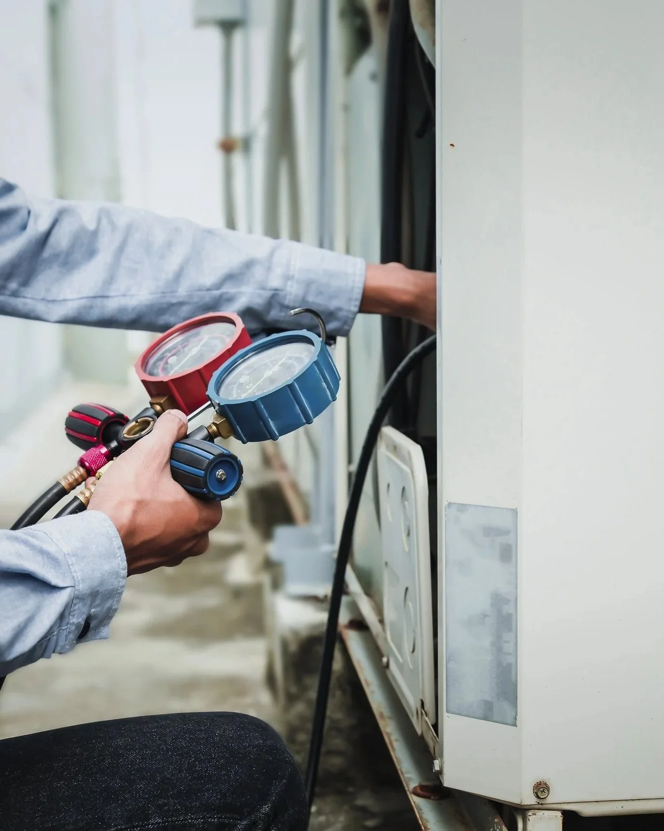 A technician is using a manifold gauge set to check refrigerant pressure on an air conditioning unit.