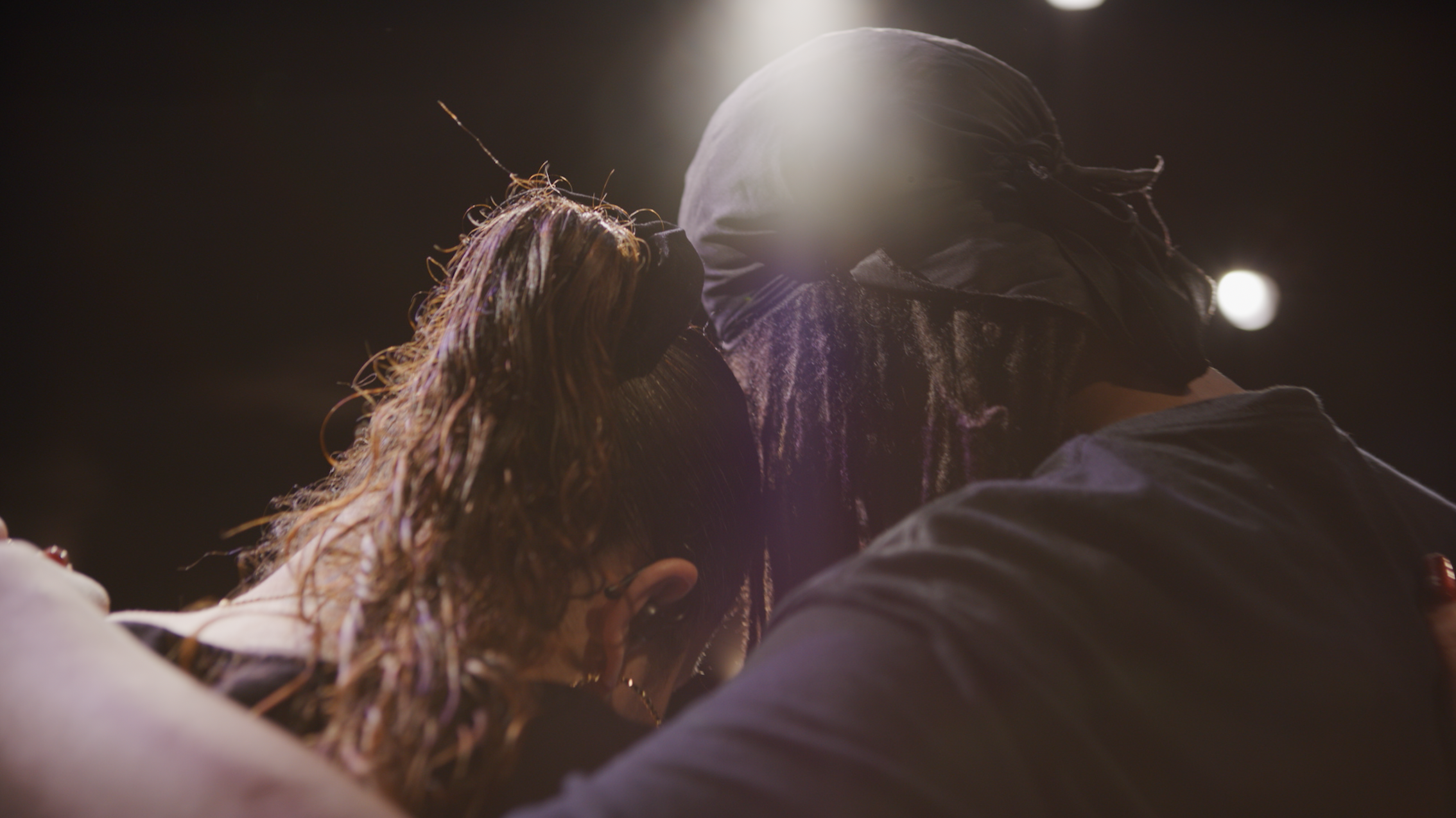 A couple with masks sharing an intimate moment at a night event, illuminated by artificial lighting.