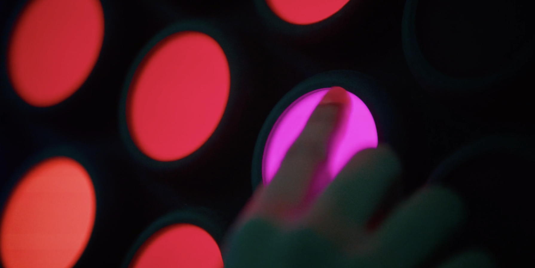 Close-up of a keyboard with illuminated pink and red keys, with a finger touching a pink key.