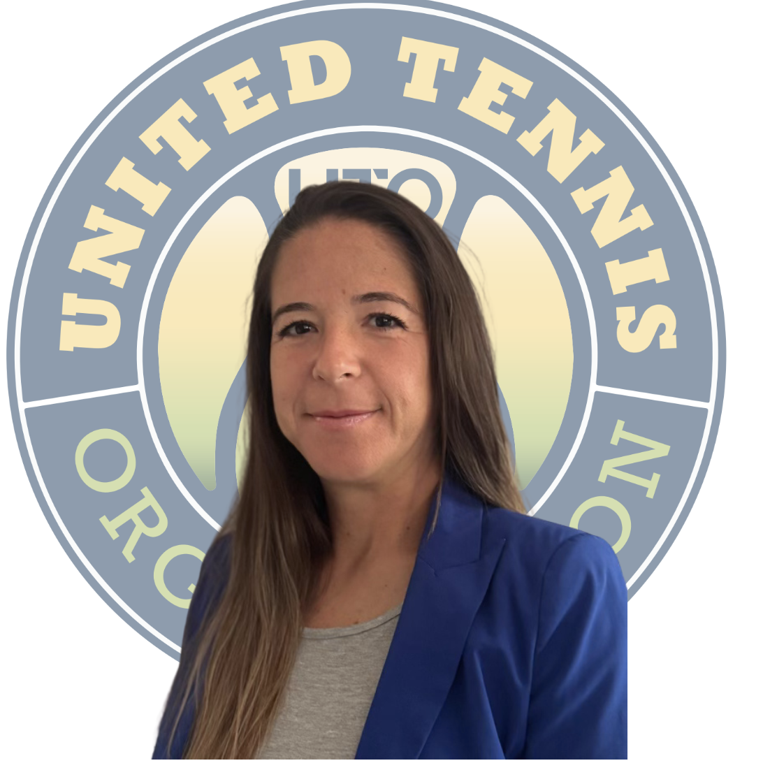 A woman with long brown hair wearing a blue blazer and gray shirt, standing in front of a blurred United Nations logo.