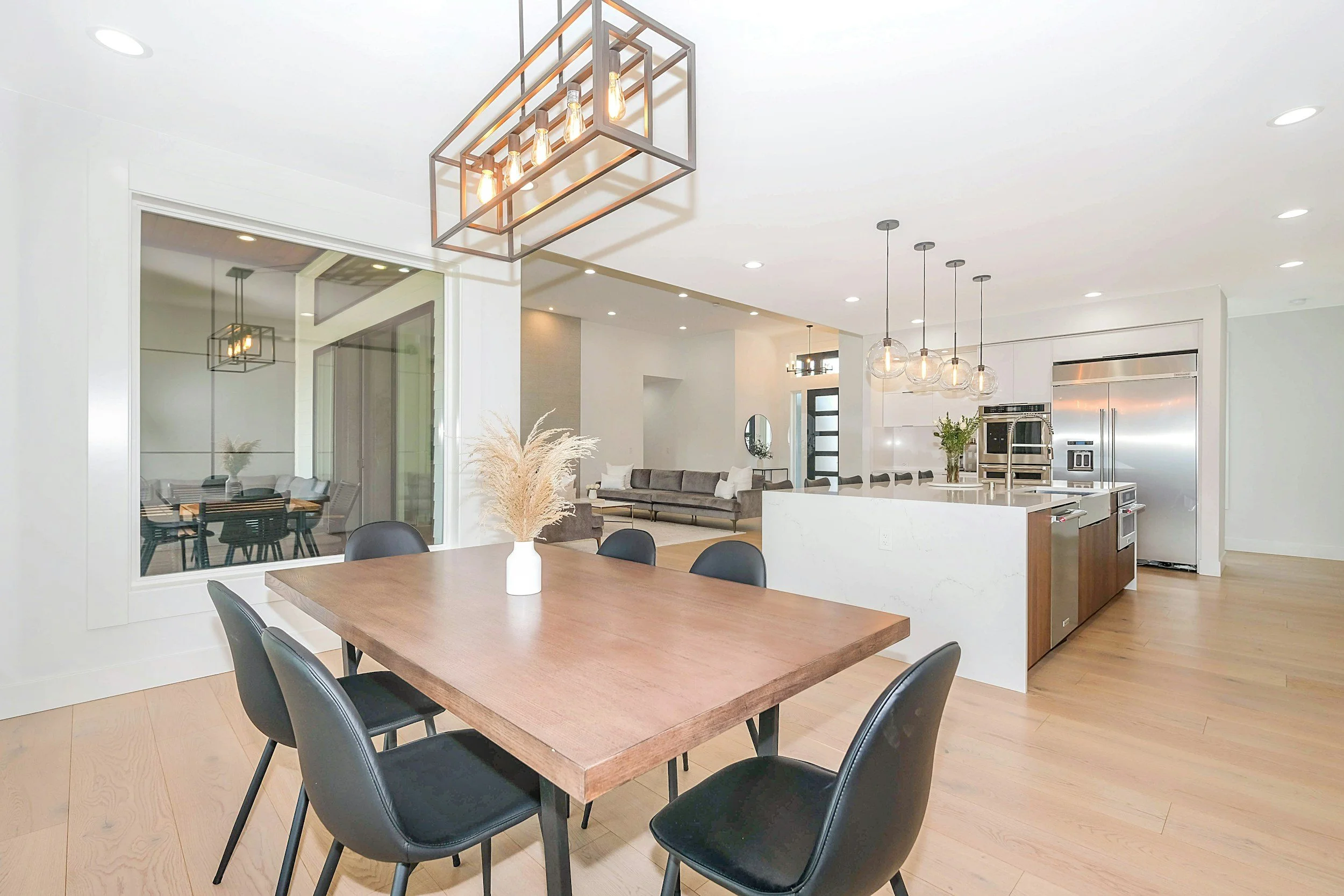 Modern open-concept kitchen and dining area with pendant lighting, a wooden dining table, black chairs, and a white kitchen island with bar stools.