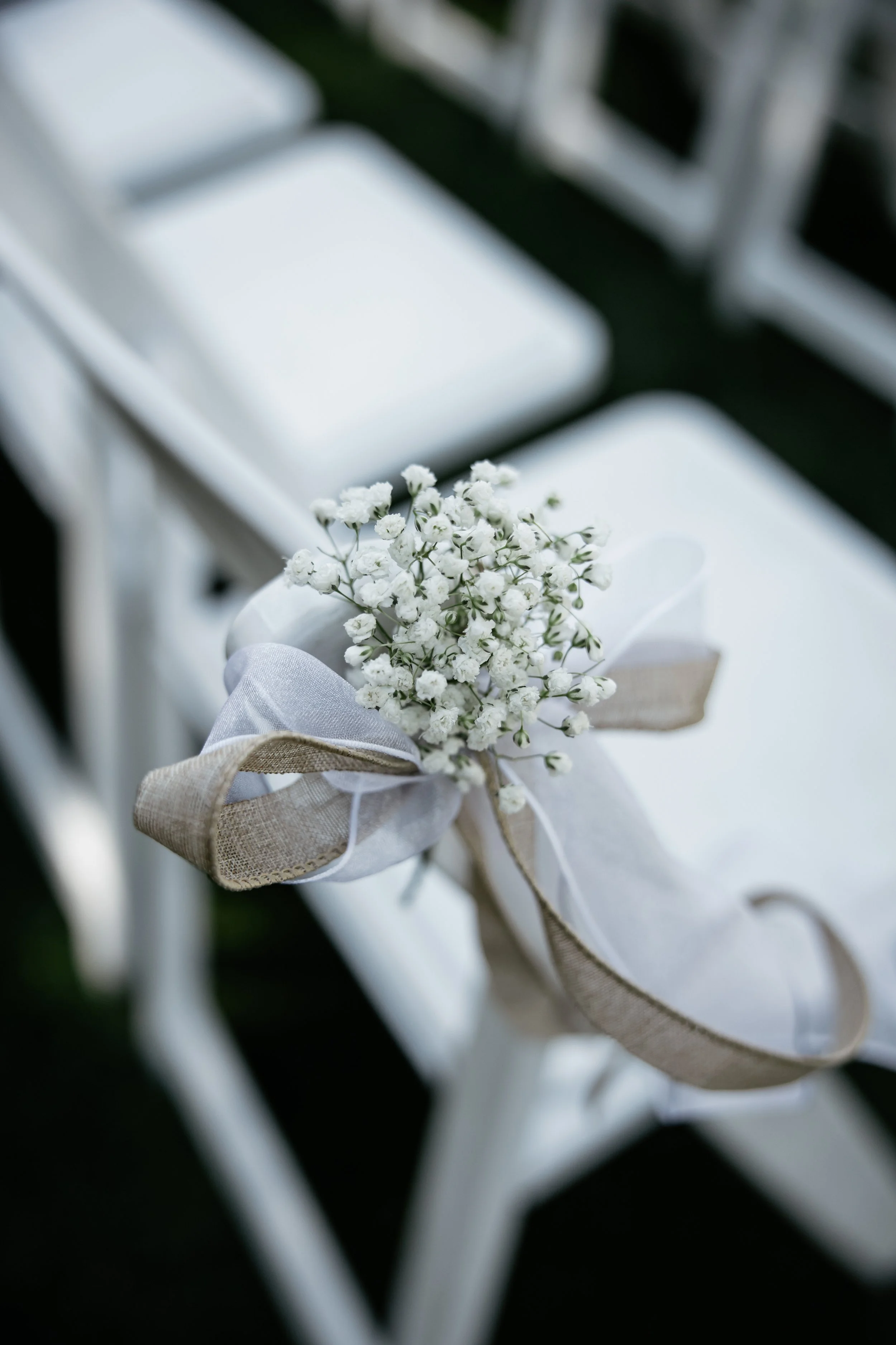 White chair decorated with a small bouquet of white flowers tied with a white and beige ribbon.