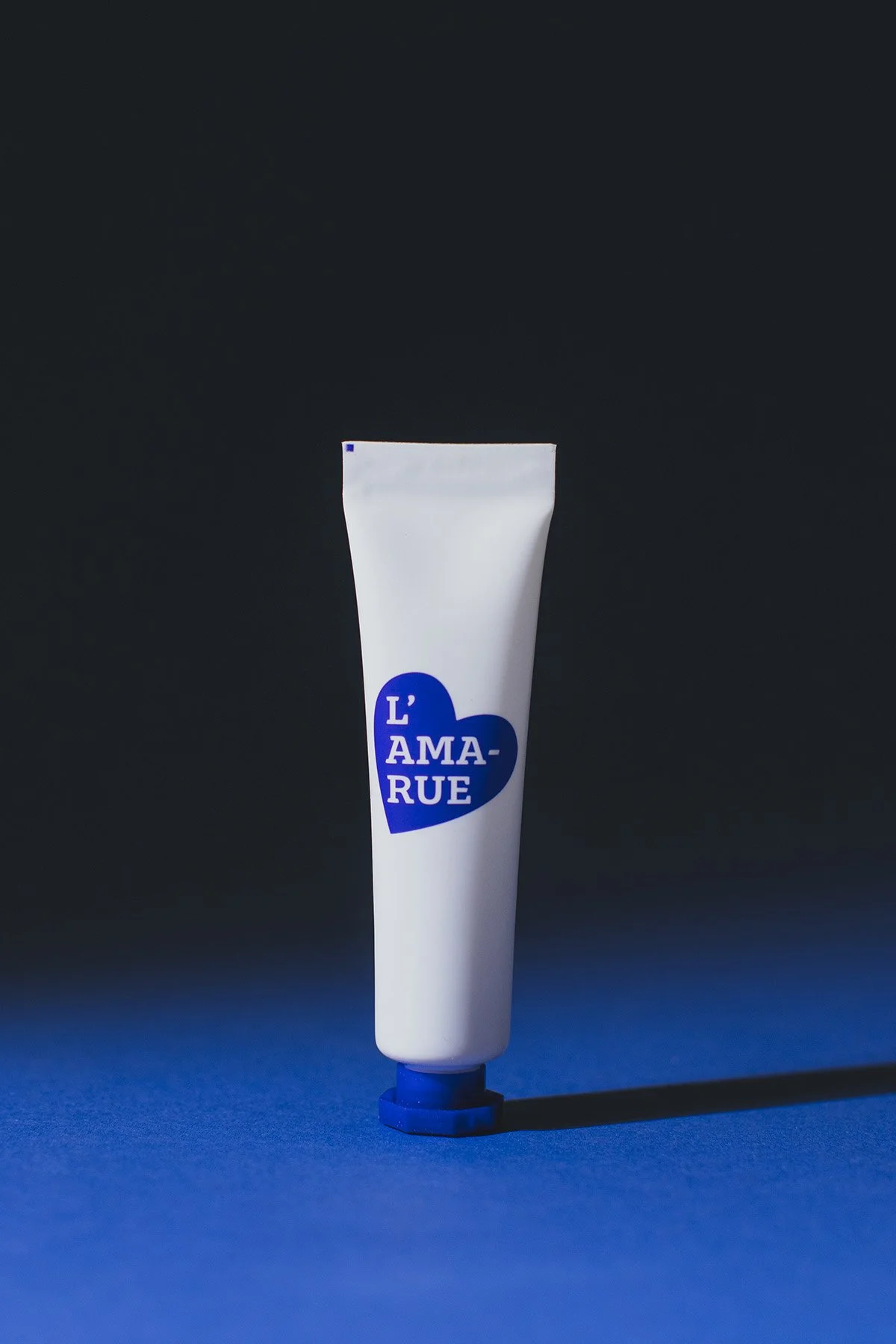 L'Amarue white tube with blue heart logo against gradient blue to black background with dramatic lighting