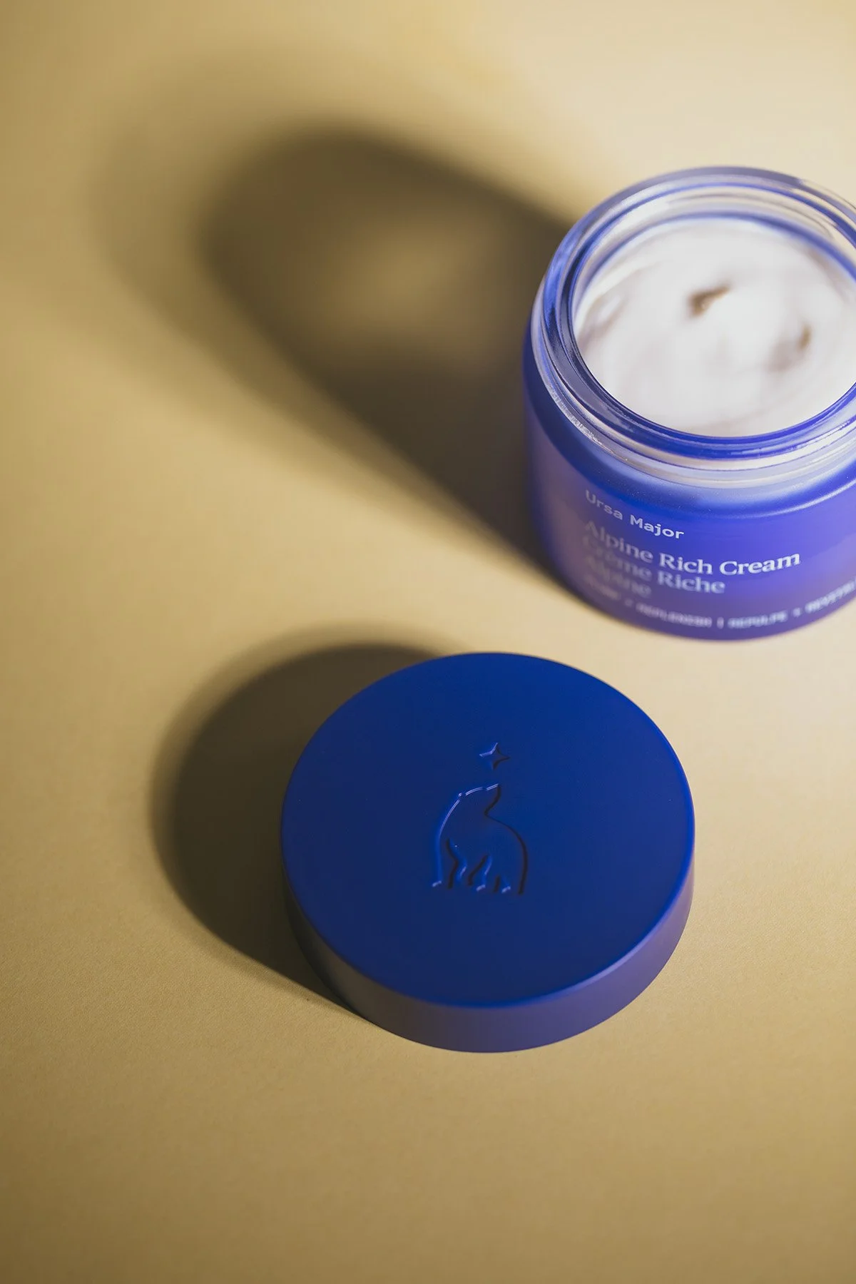 Ursa Major Alpine Rich Cream jar with lid displaying embossed bear logo against warm beige background with soft shadows