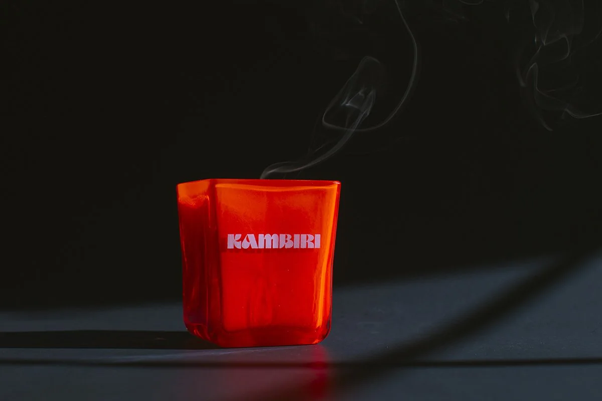 Dramatic product photography of glowing red Kambiri branded candle with wispy smoke against dark moody background
