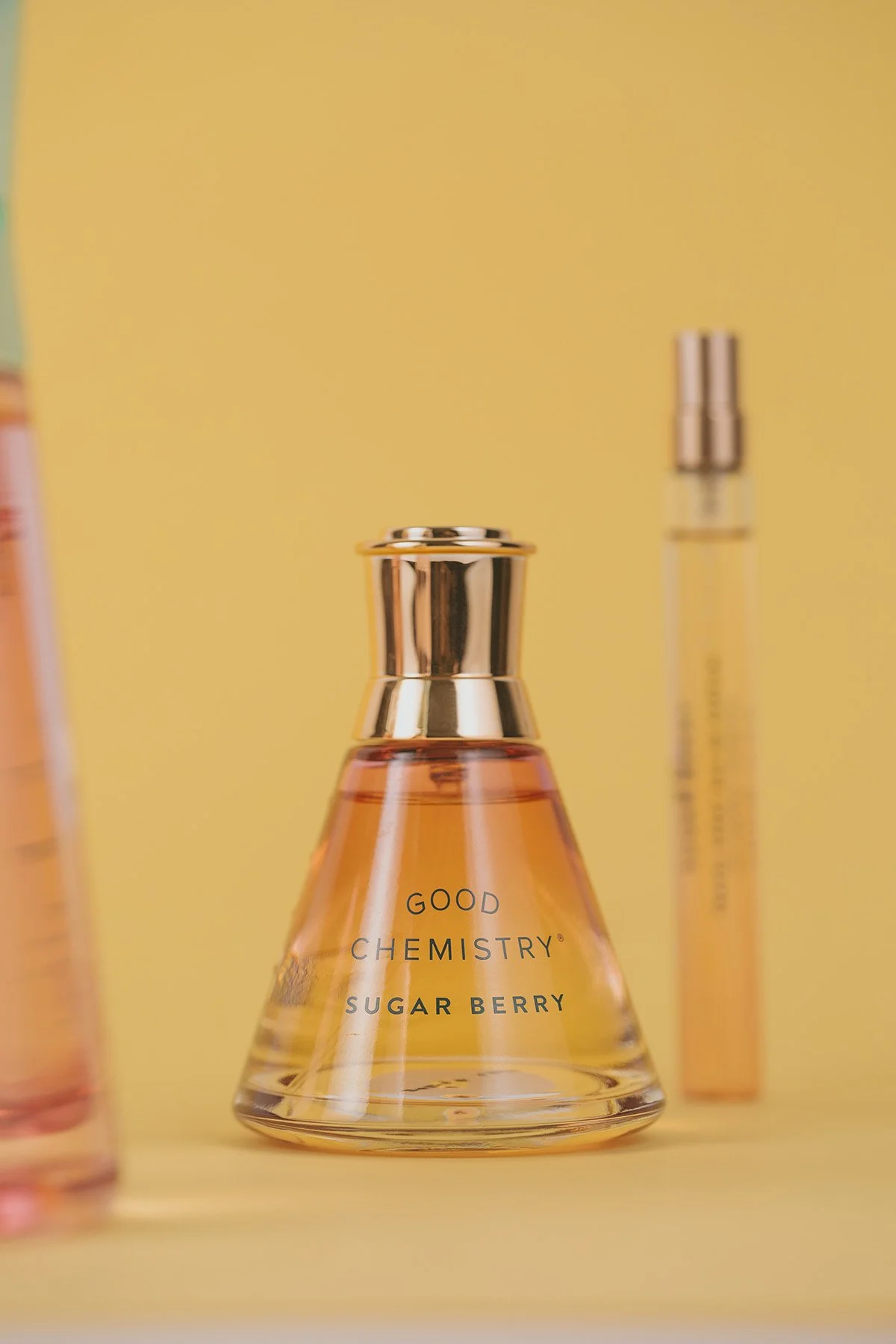 Good Chemistry Sugar Berry perfume bottle with gold cap and amber liquid against soft yellow background with blurred fragrance bottles