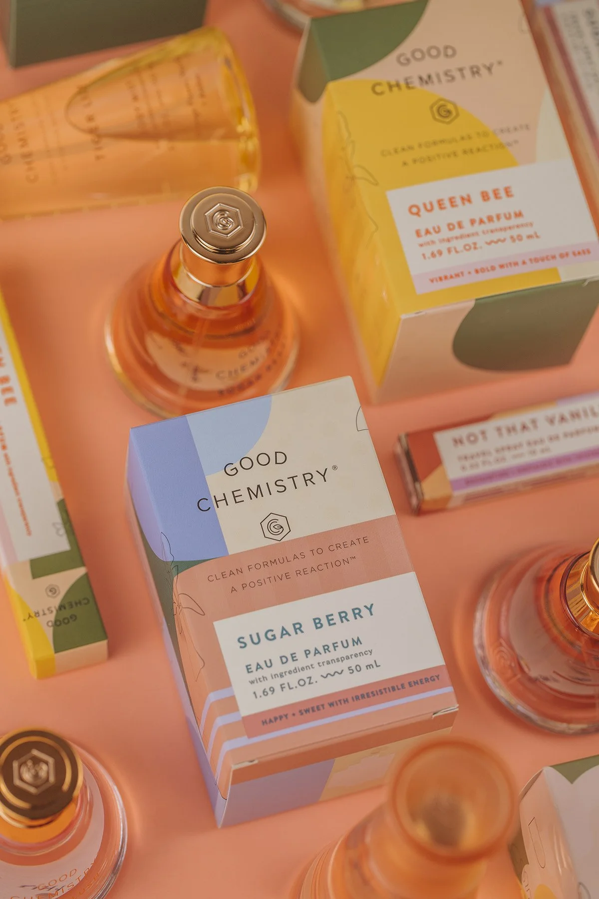 Warm-toned flat lay of Good Chemistry Sugar Berry eau de parfum with glass bottle and colorful product packaging including Queen Bee scent