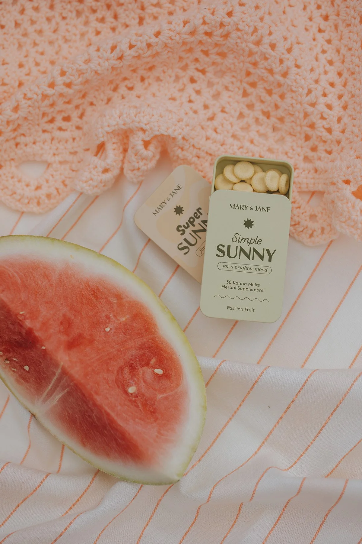 Mary & Jane Simple Sunny passion fruit kanna melts herbal supplement tin on striped towel with watermelon slice and textured scrunchie