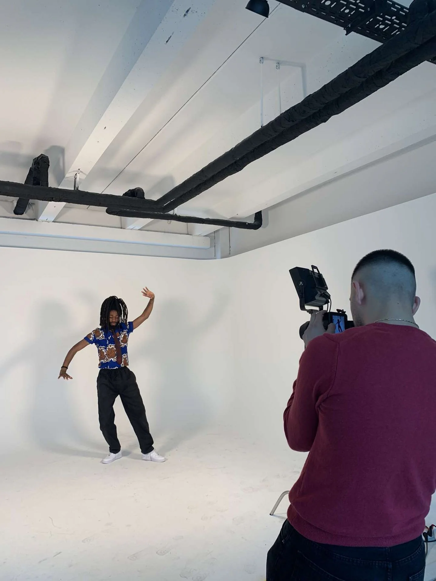 Sandro macht ein Fotoshooting im Fotostudio, während ein Mann auf der weißen Studio-Hintergrund tanzt.