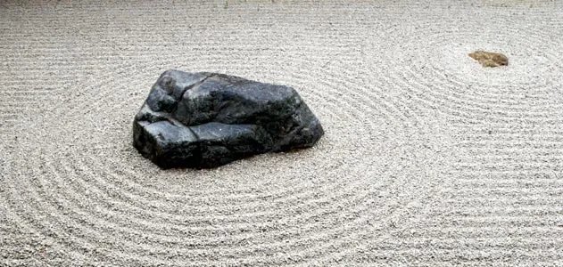 A large black rock in a Japanese Zen garden with a raked gravel pattern encircling it.