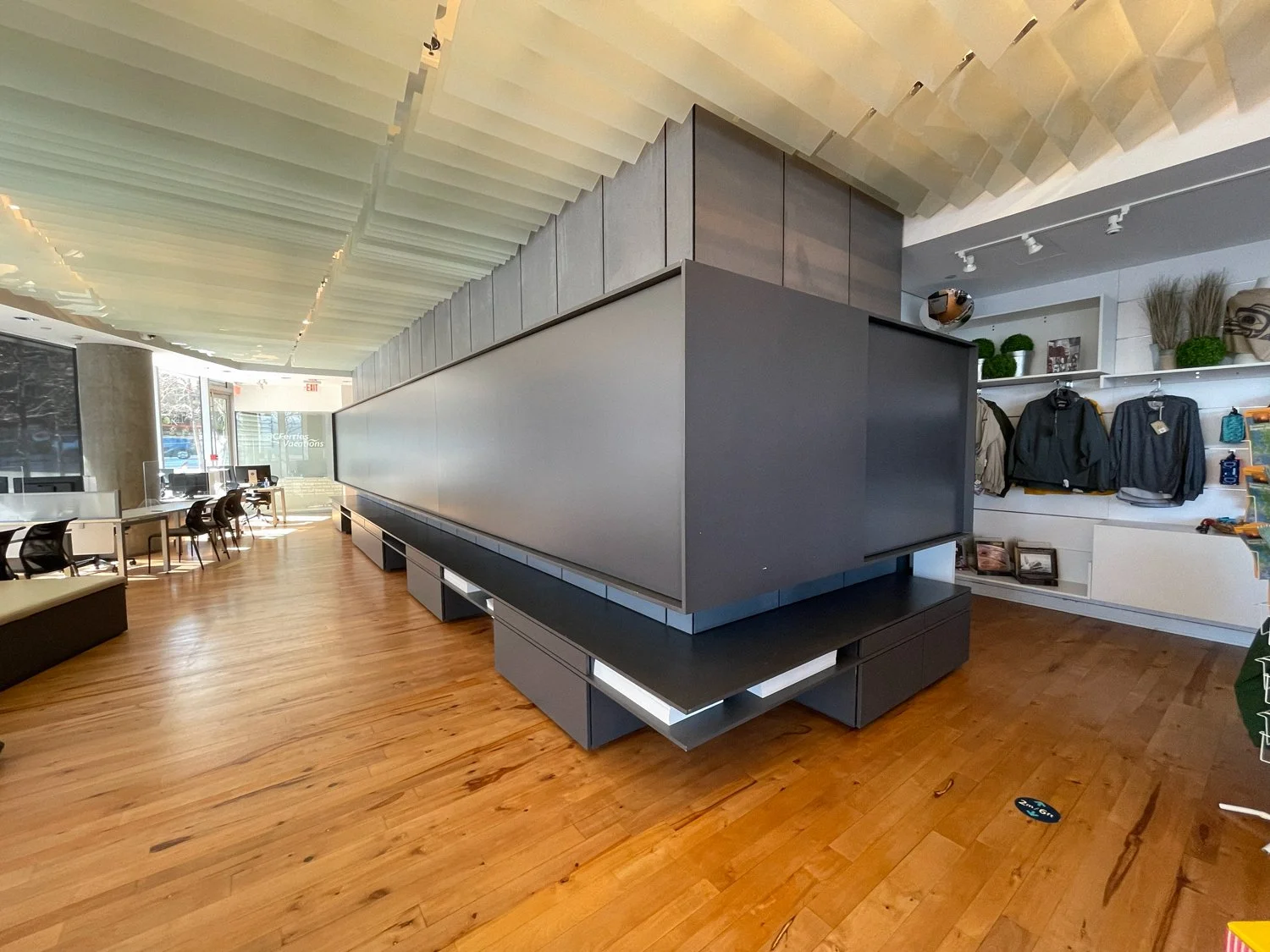 Interior of a modern retail store with wooden flooring, black display fixtures, and clothing on shelves.