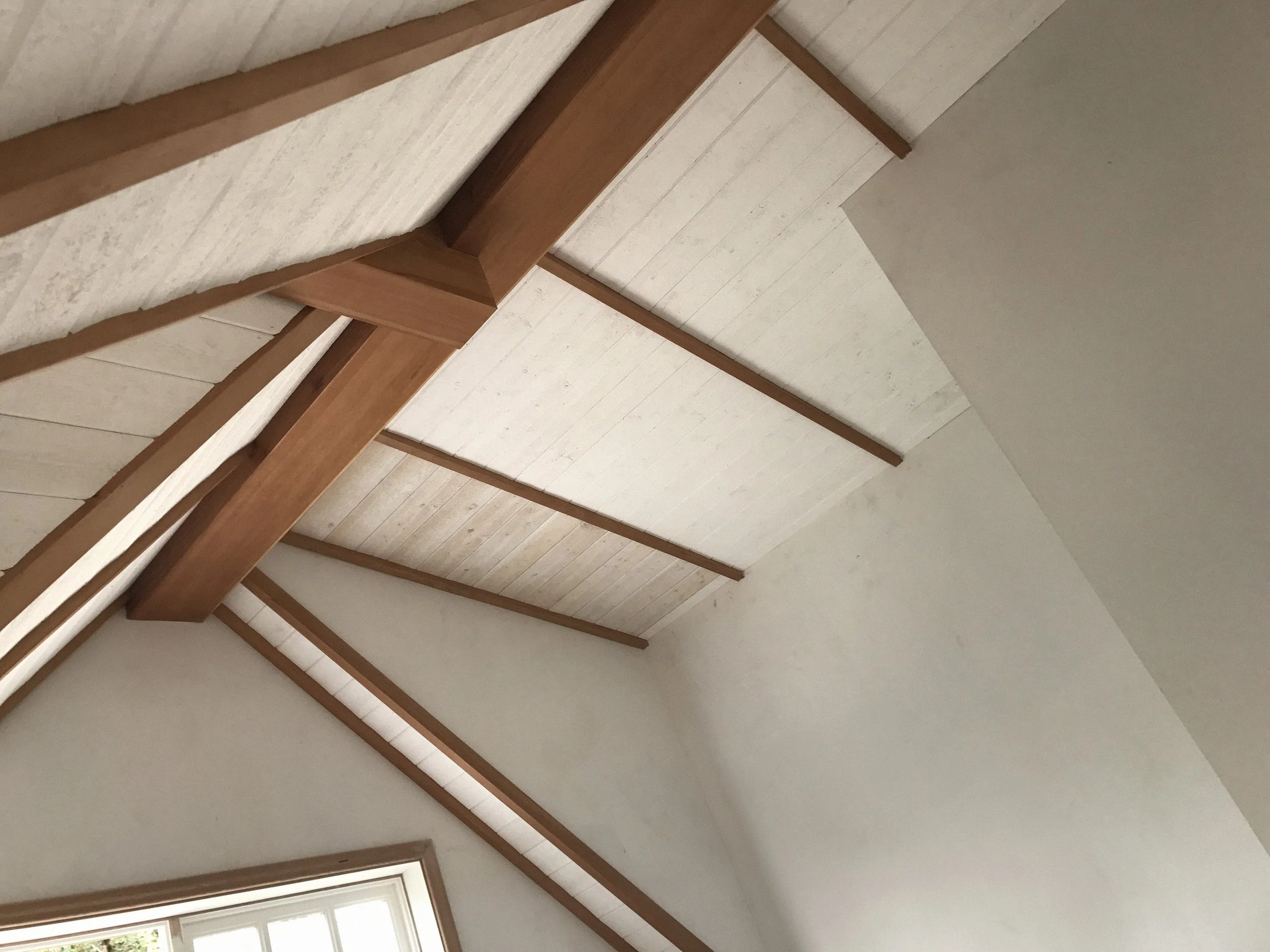 Close-up view of a sloped ceiling with exposed wooden beams and painted white wooden panels.