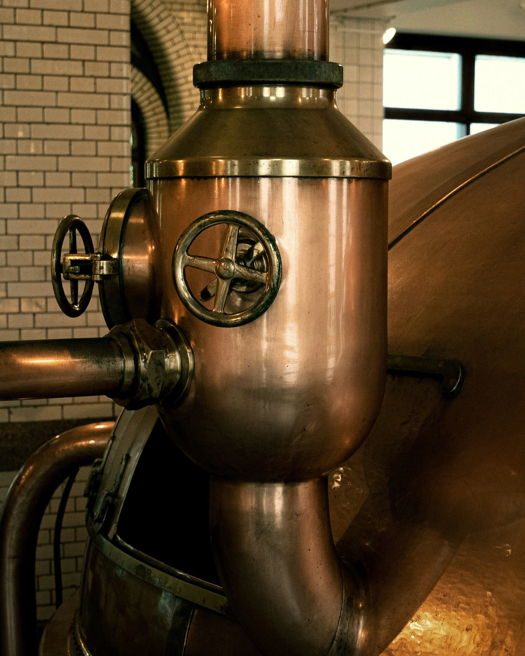 Close-up of a large industrial copper brewing or distilling machine with valves and pipes.