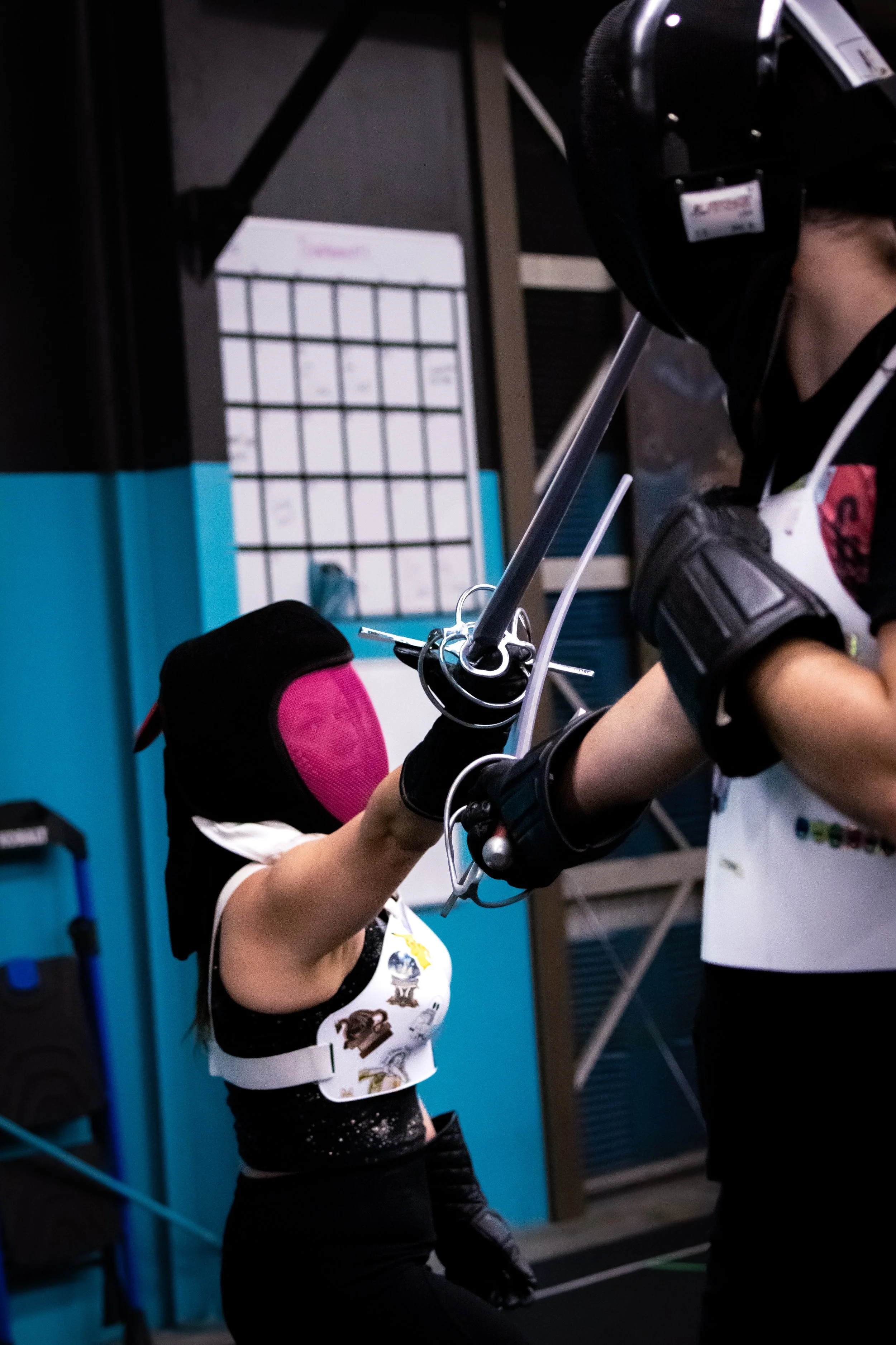 Two people practicing fencing with swords in a martial arts dojo, wearing protective gear including masks and padded clothing.