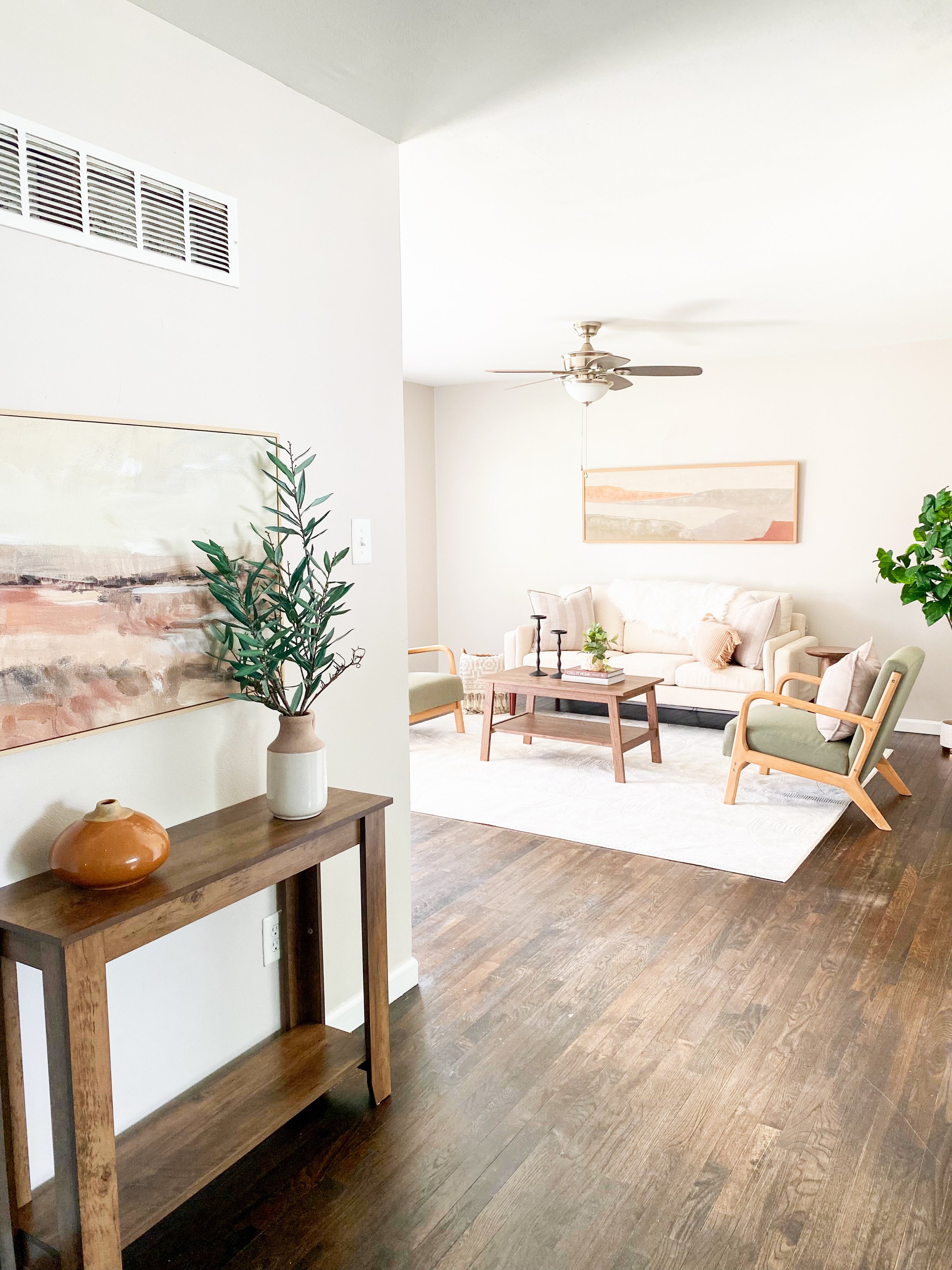 March Home Staging St. Louis, Living room with beige sofa, green armchairs, wooden coffee table, ceiling fan, artwork on wall, indoor plants, and hardwood floors.