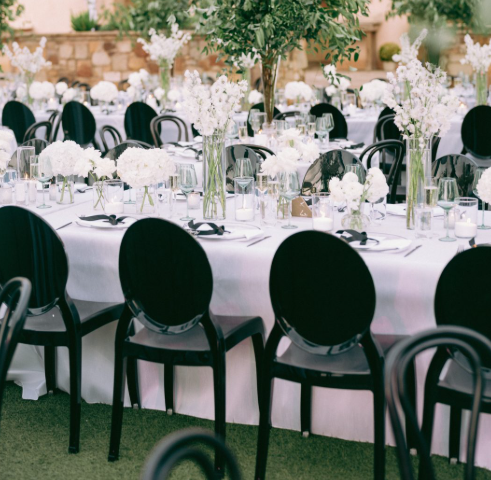 Elegant outdoor event setup with round tables, white tablecloths, floral centerpieces, and black chairs.