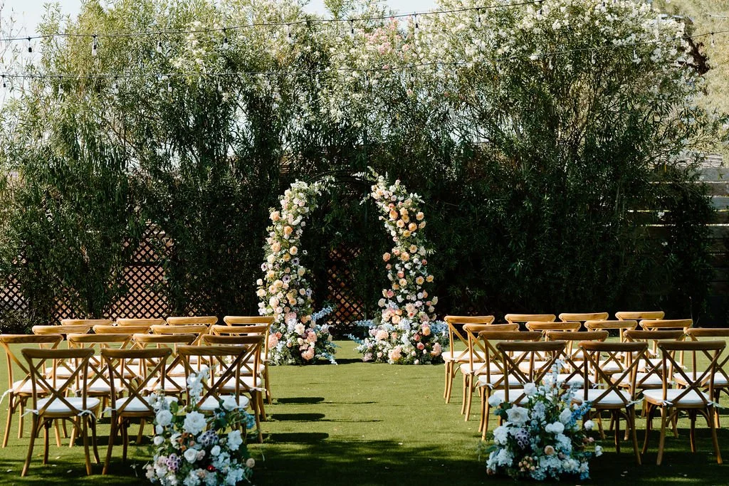 Outdoor wedding ceremony setup with floral arch and chairs on a grassy area