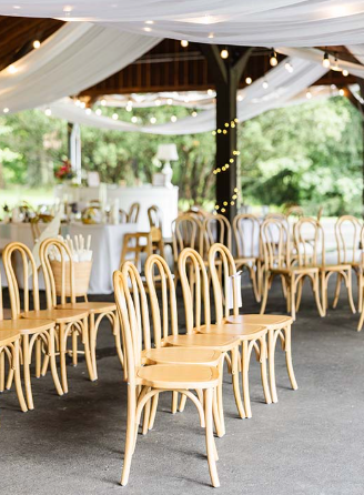 Natural bentwood chairs arranged in ceremony rows under an outdoor decorated tent at a wedding or event venue.