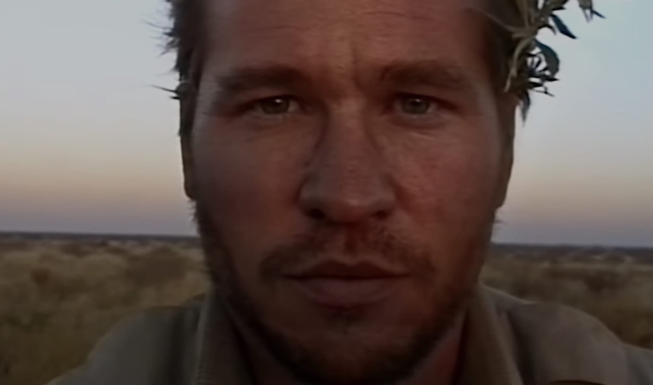 Close-up of a man with wet hair and dirty face in an arid landscape during sunset