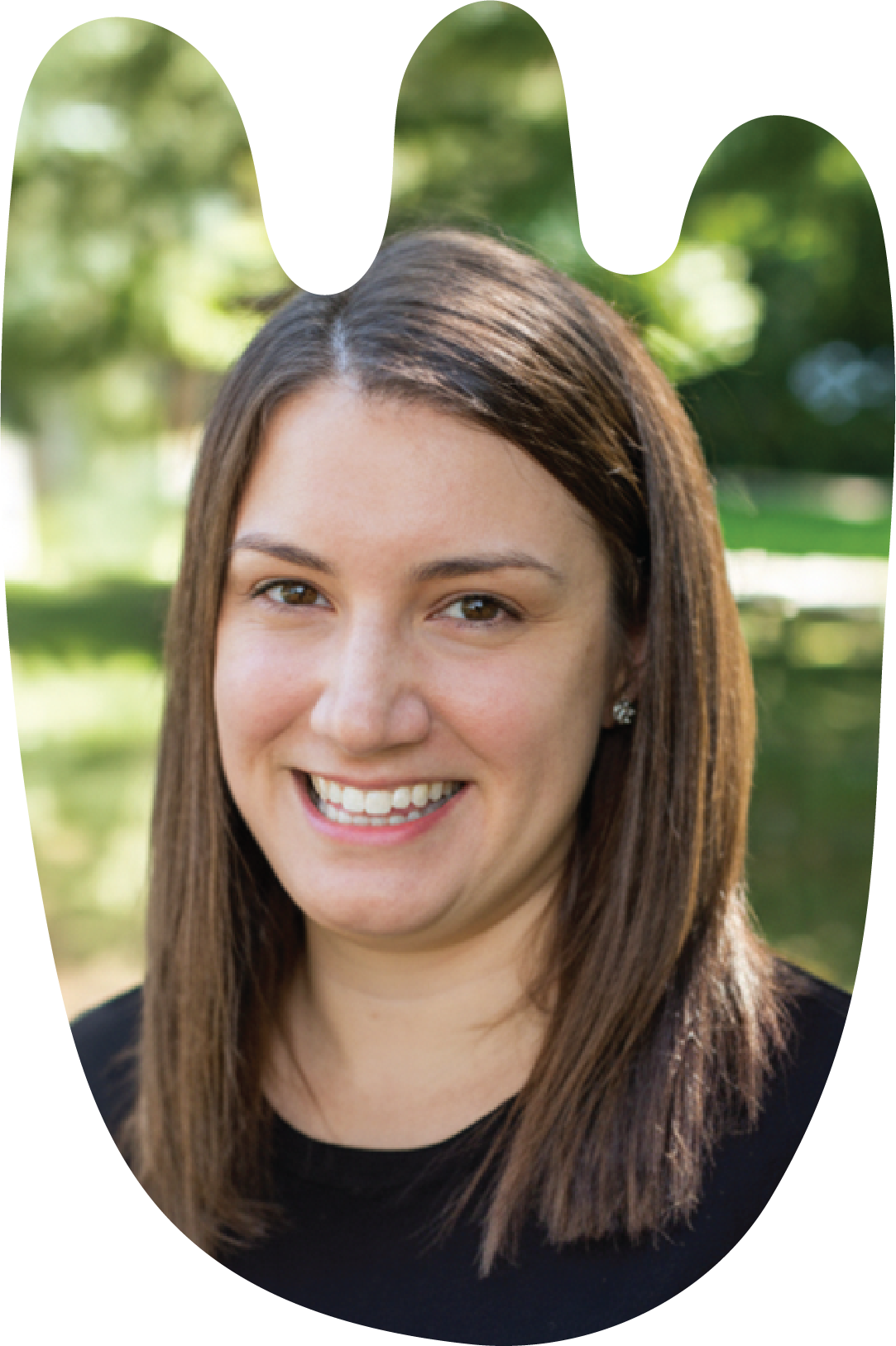 Dr. Ami Tint has a bright smile, brown hair and small flower earrings. behind her out of focus is an urban park. The photo is cropped into the loose shape of a tulip.