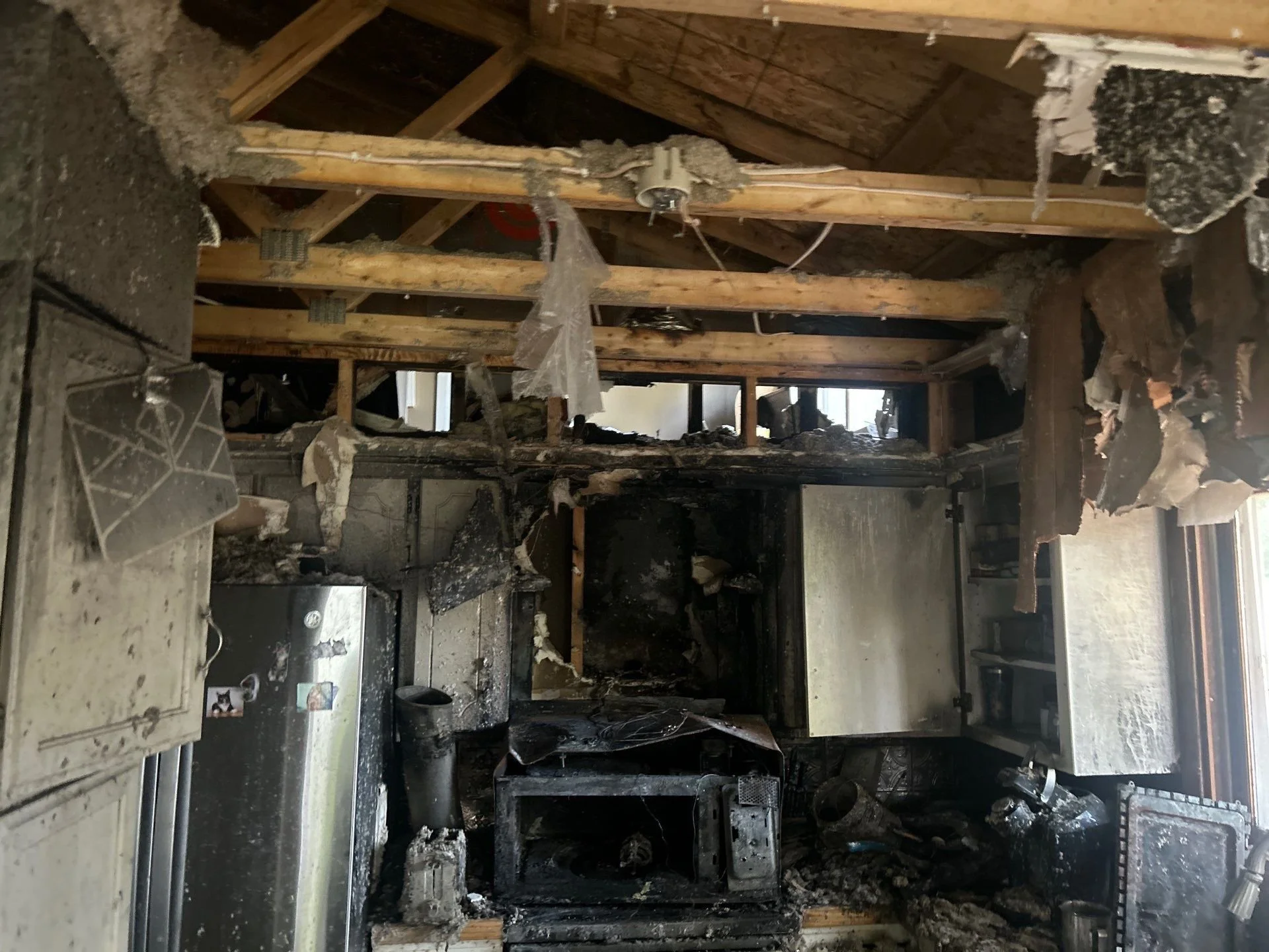 Kitchen with severe fire damage, burnt cabinets, and charred debris scattered across countertops.