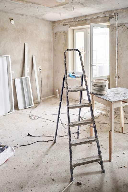Room under renovation with construction tools, including a stepladder, window frames, and a table with construction materials.