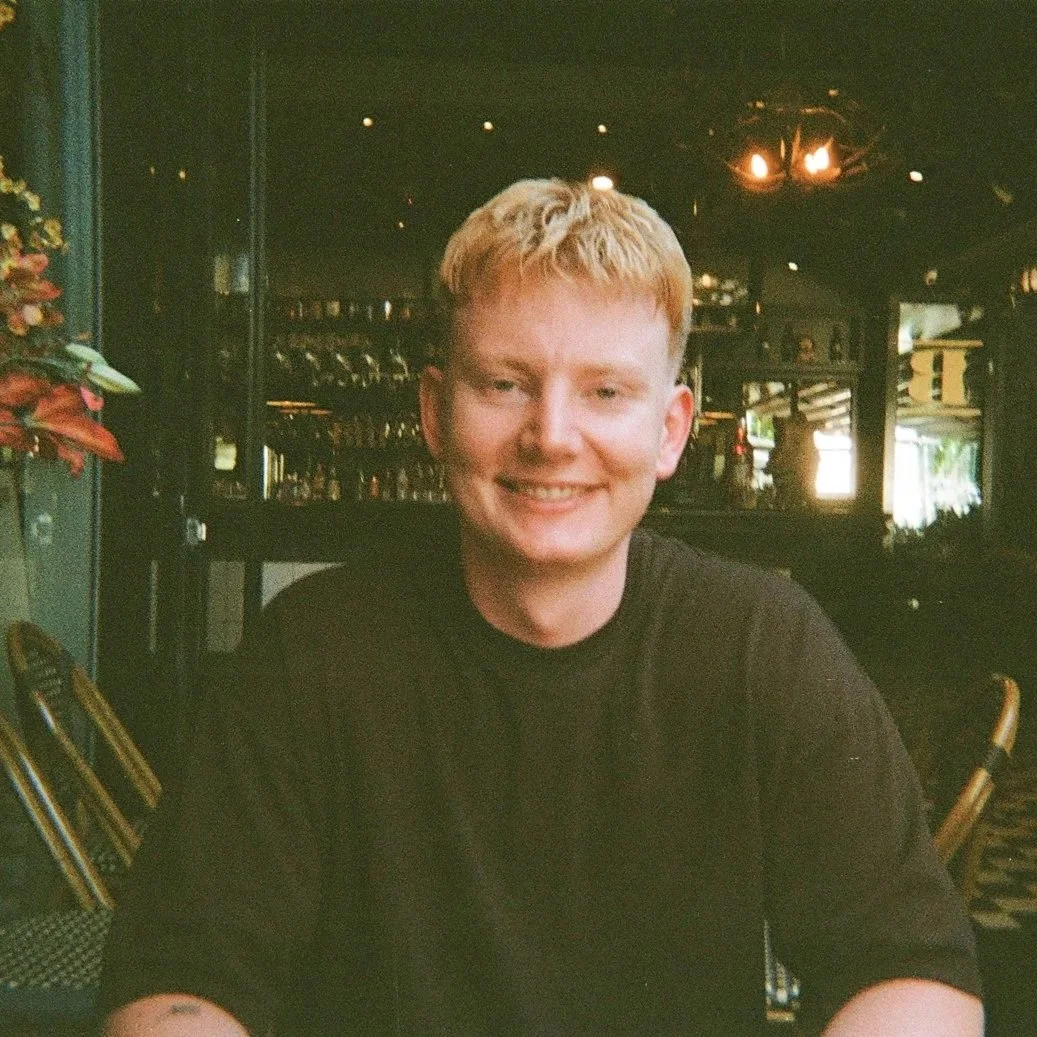 A young man with blond hair smiling at a restaurant or cafe.
