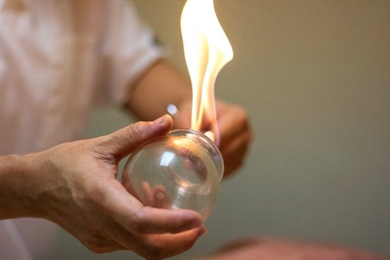 A person holding a clear glass orb with fire burning inside it.