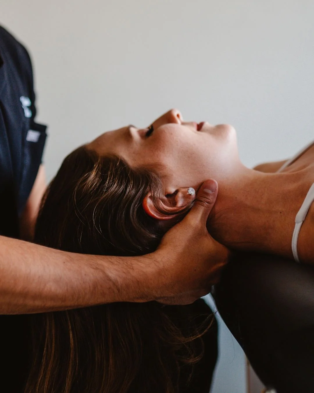 A woman receiving a manual therapy or chiropractic adjustment on her neck and head from a practitioner in a clinical setting.