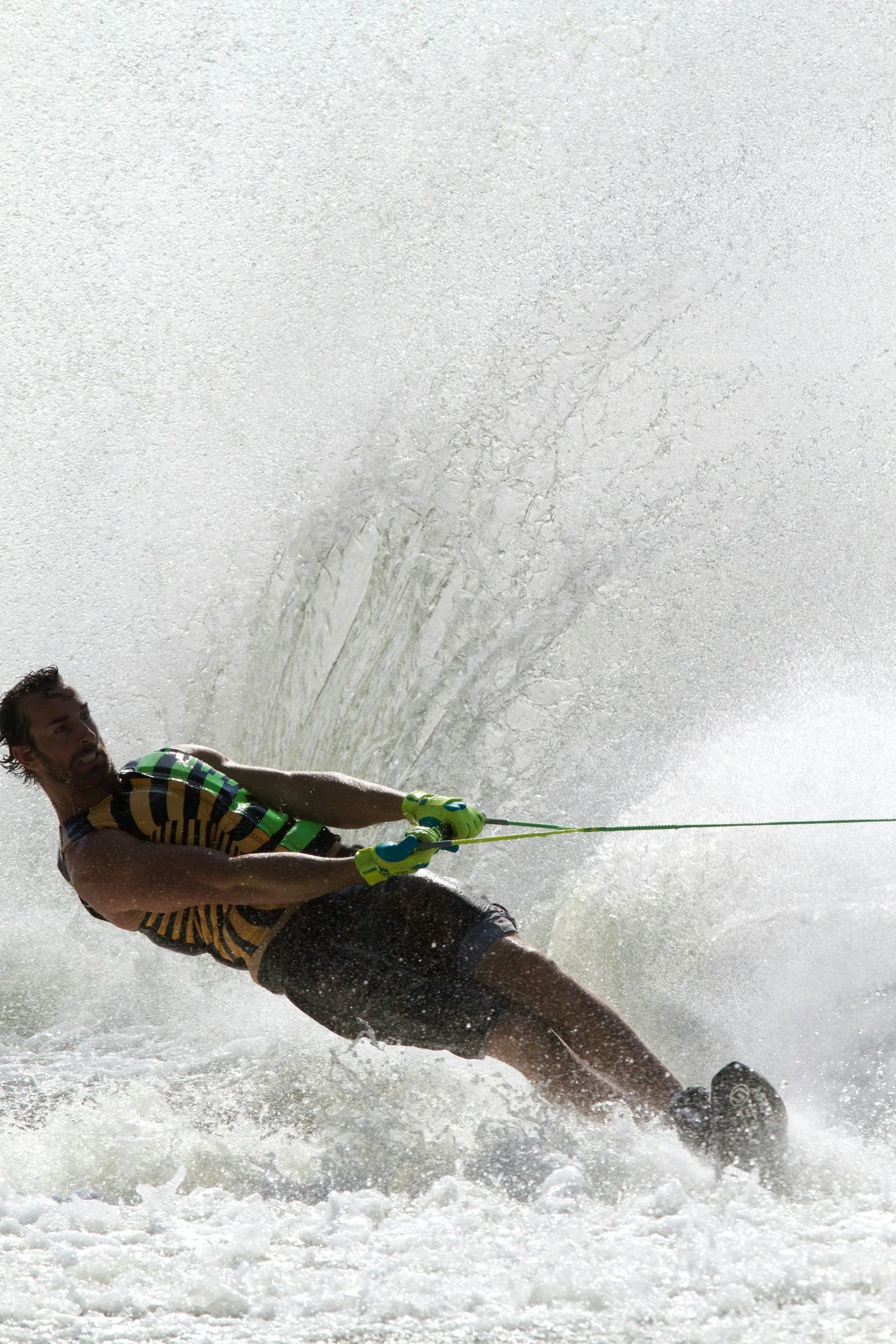 Moree Water Ski Club A man is water skiing on a body of water. He is holding onto a tow rope and is wearing a striped shirt, shorts, and gloves. Water is splashing around him as he skims across the water's surface.