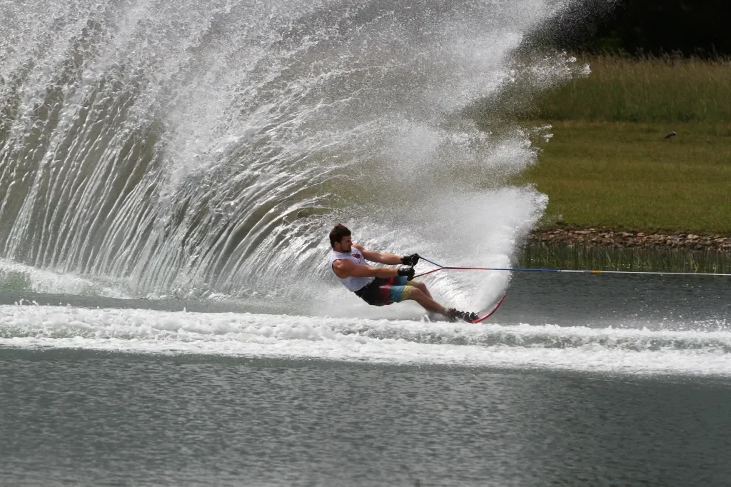 A man water skiing on a lake, creating a large splash behind him.