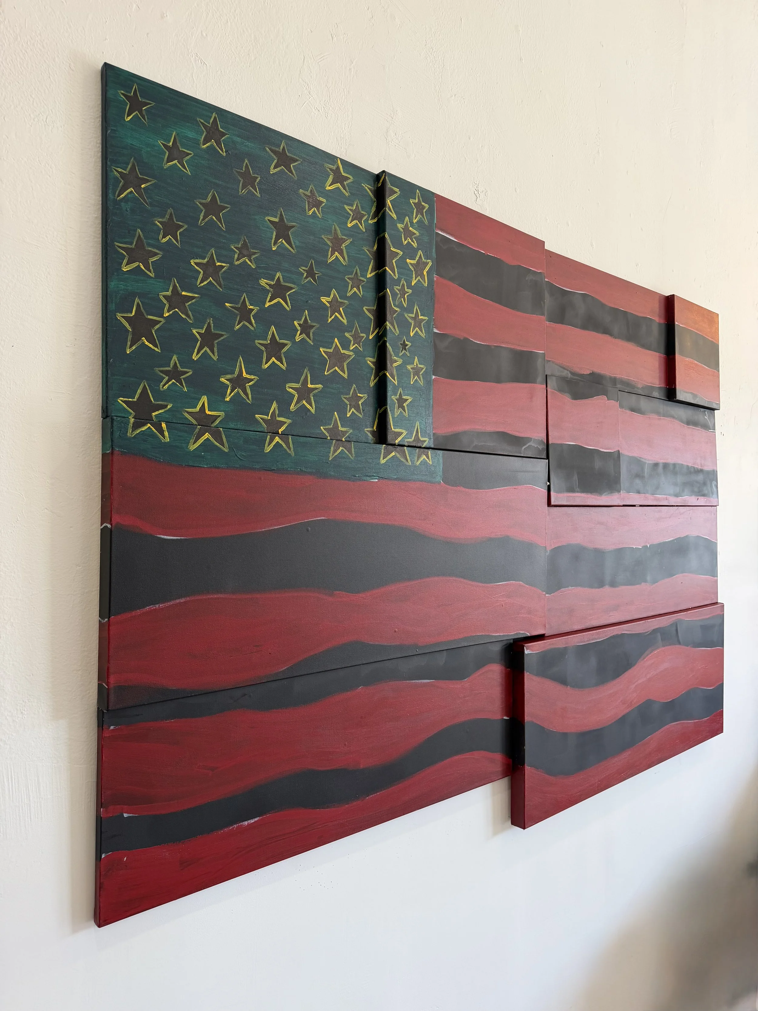 Wooden art piece painted with an American flag design, featuring stars and red and gray stripes, mounted on a white wall.