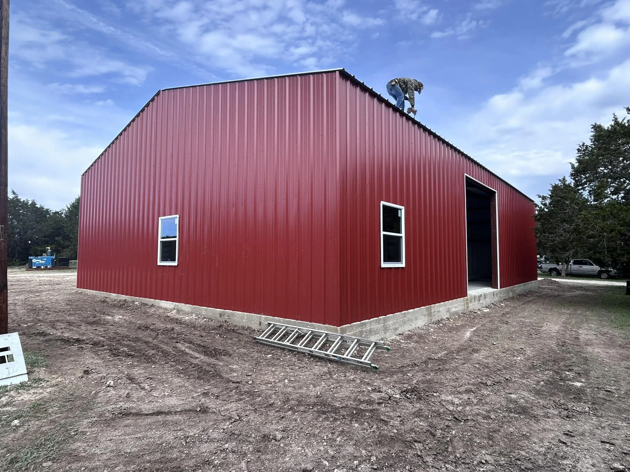 A person working on the roof of a red metal building under a partly cloudy sky.