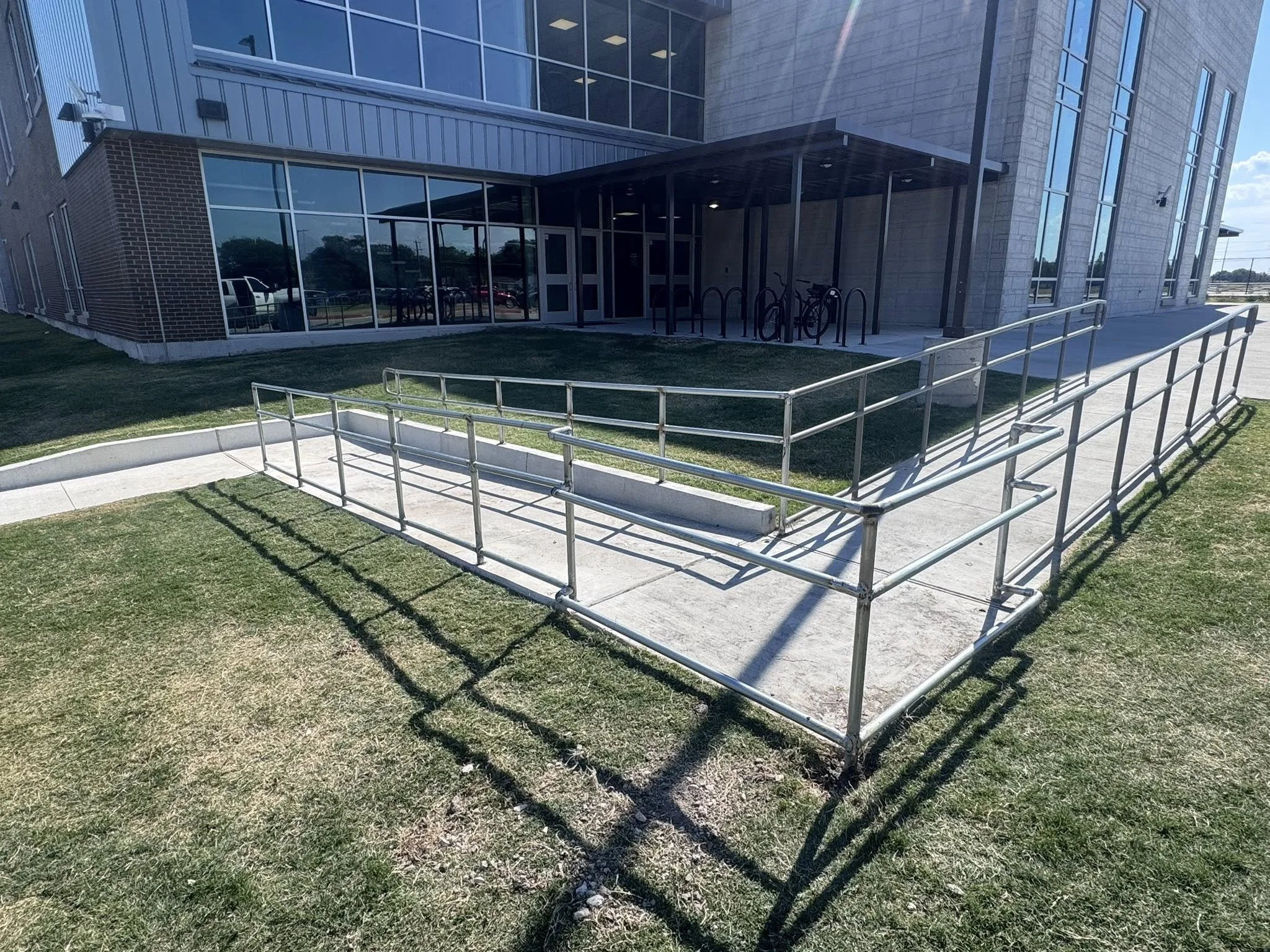 Accessibility ramp with metal handrails leading to the entrance of a modern building with glass windows and brick walls.