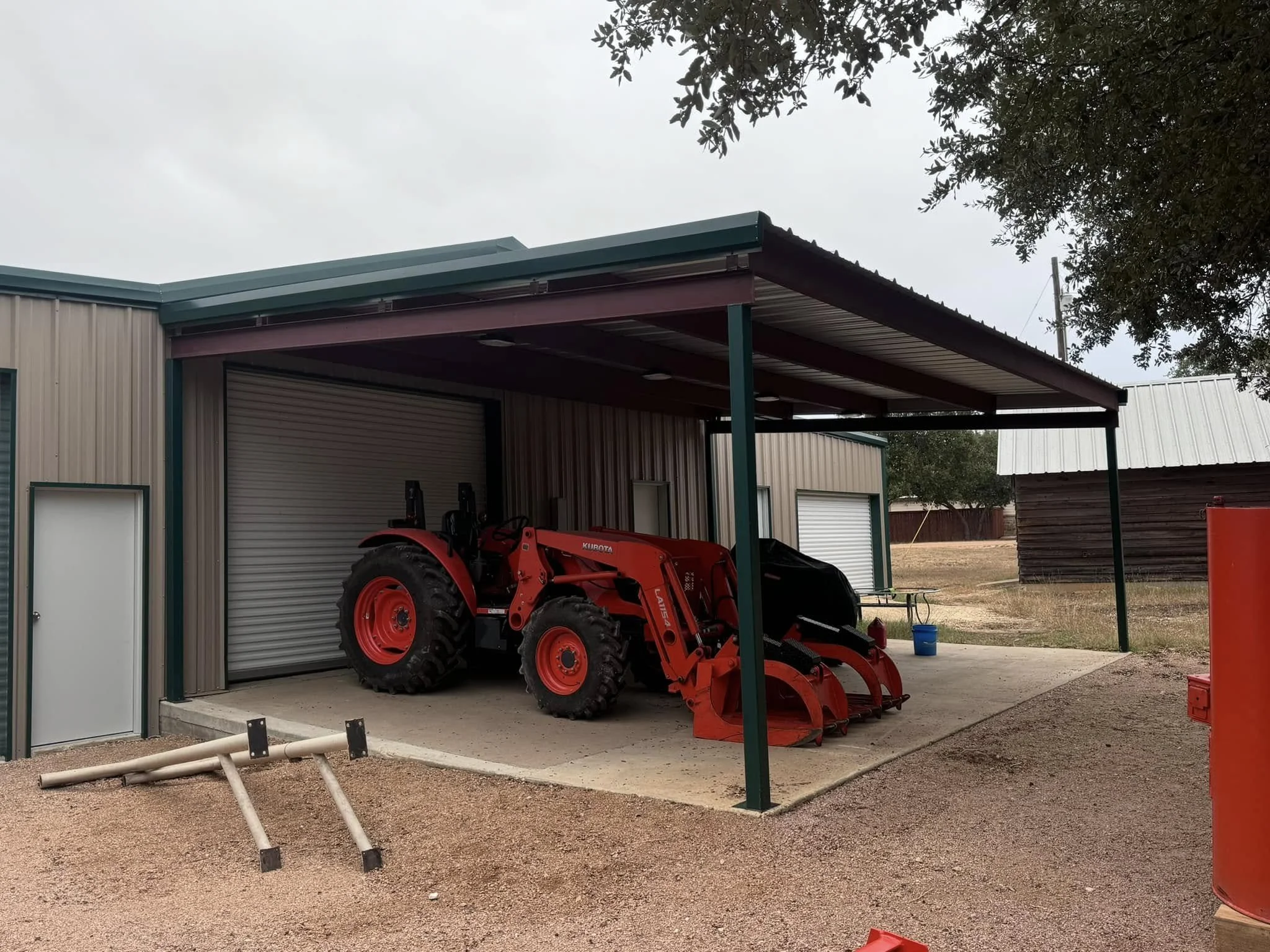 Red tractor with front loader attachment parked under a metal carport at a farm or rural property.