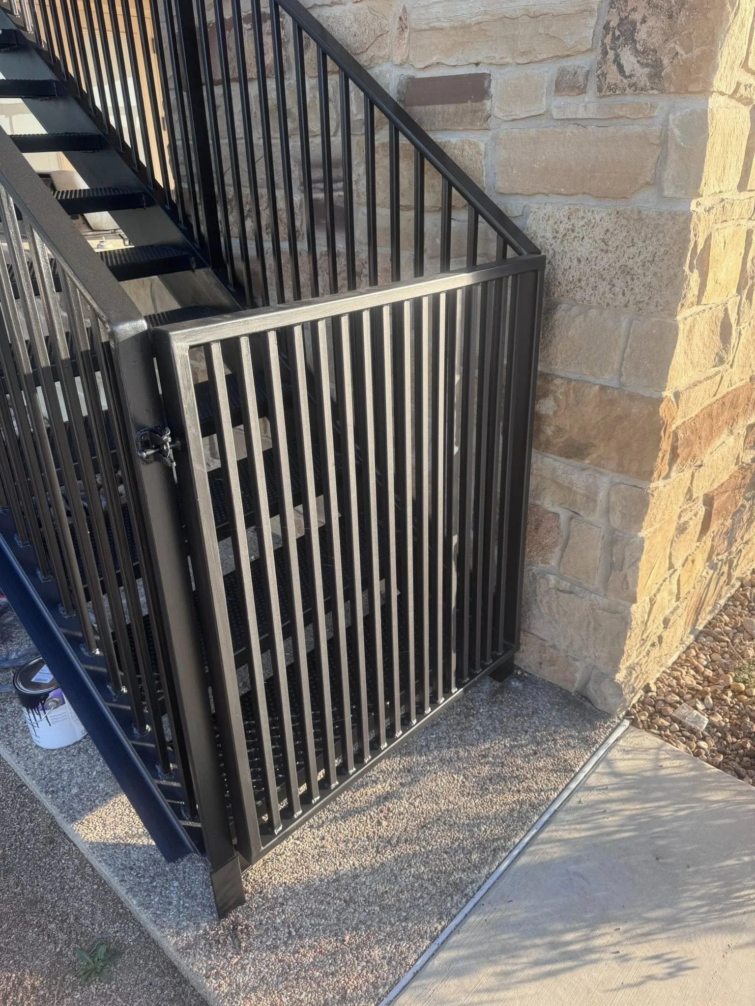 Black metal stair lift with safety gate installed on an outdoor stairwell next to a brick wall.