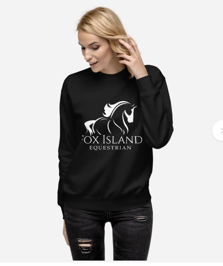 A woman wearing a black sweatshirt with a white horse logo and the text 'OXY ISLAND EQUESTRIAN' printed on it.