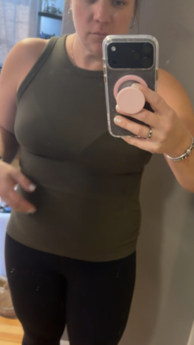 A woman taking a mirror selfie with a smartphone in a casual outfit of a sleeveless top and black leggings