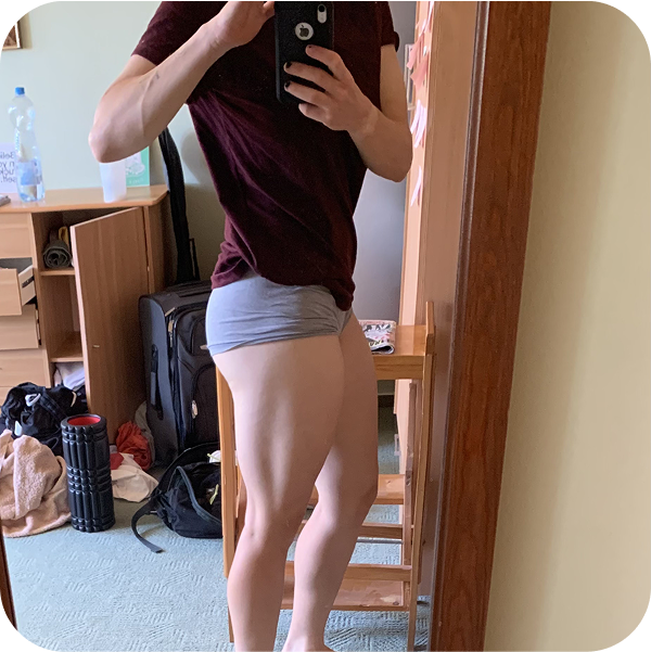 A person taking a mirror selfie, showing their leg muscles in a room with luggage and personal items.