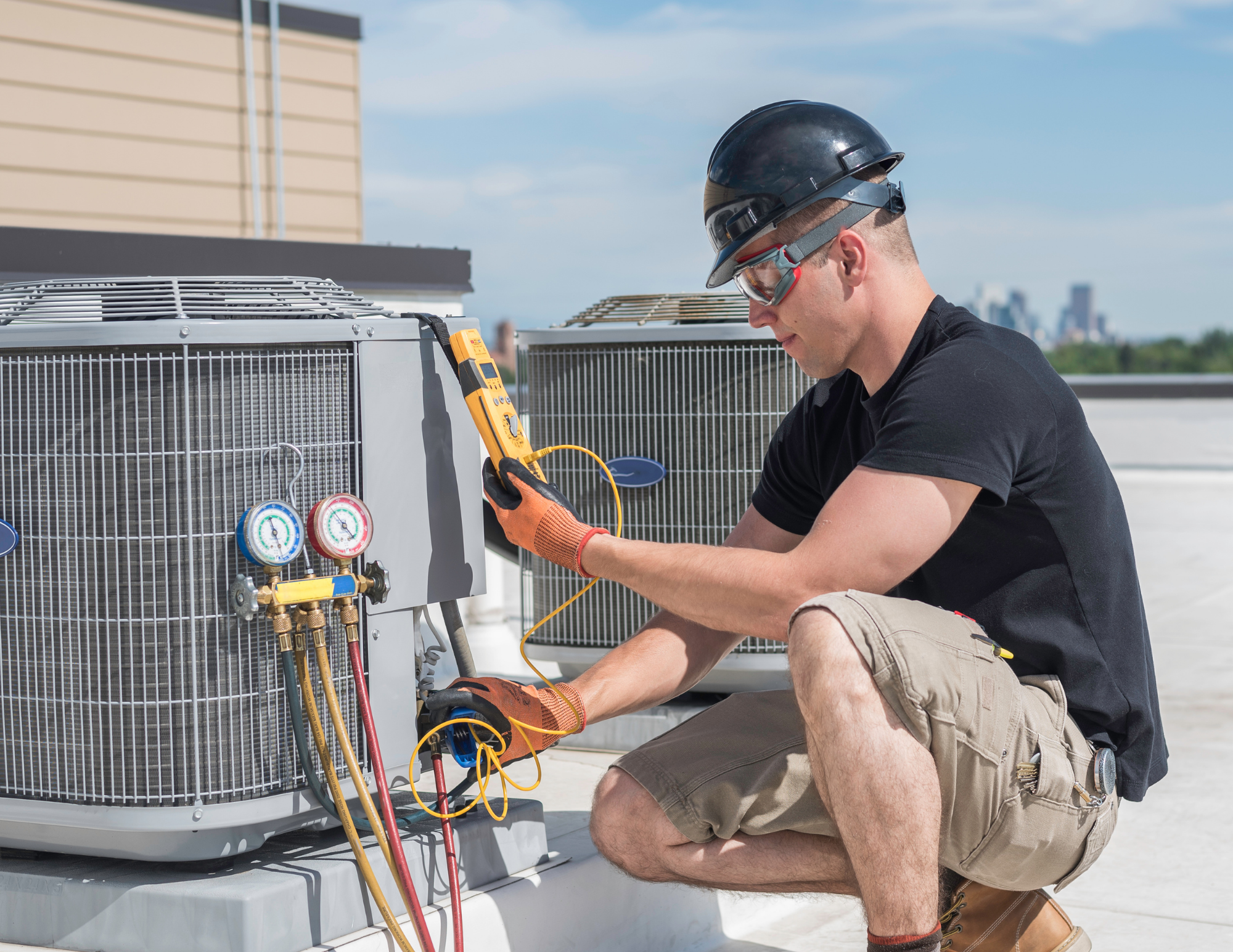 A technician wearing a safety helmet, goggles, and gloves is repairing or maintaining an air conditioning unit on a rooftop, using a multimeter and various tools, with a cityscape visible in the background.